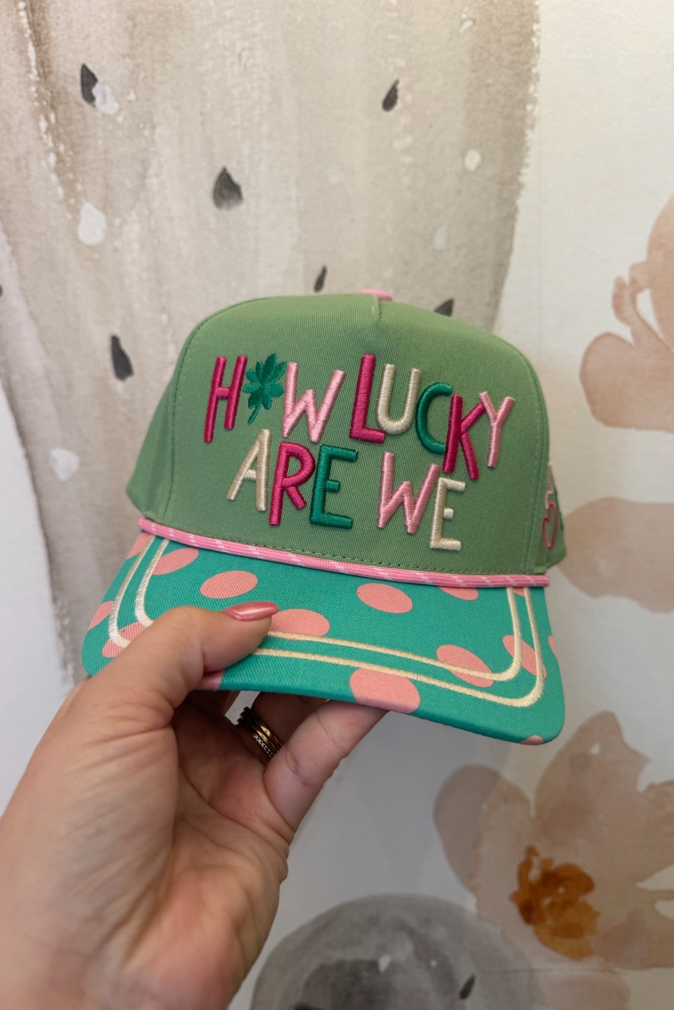 Green cap with colorful text held by a hand against a patterned background
