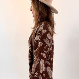 Person wearing a brown patterned sweater and beige hat on a white background