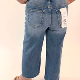 Person wearing blue jeans with a tag on a plain background