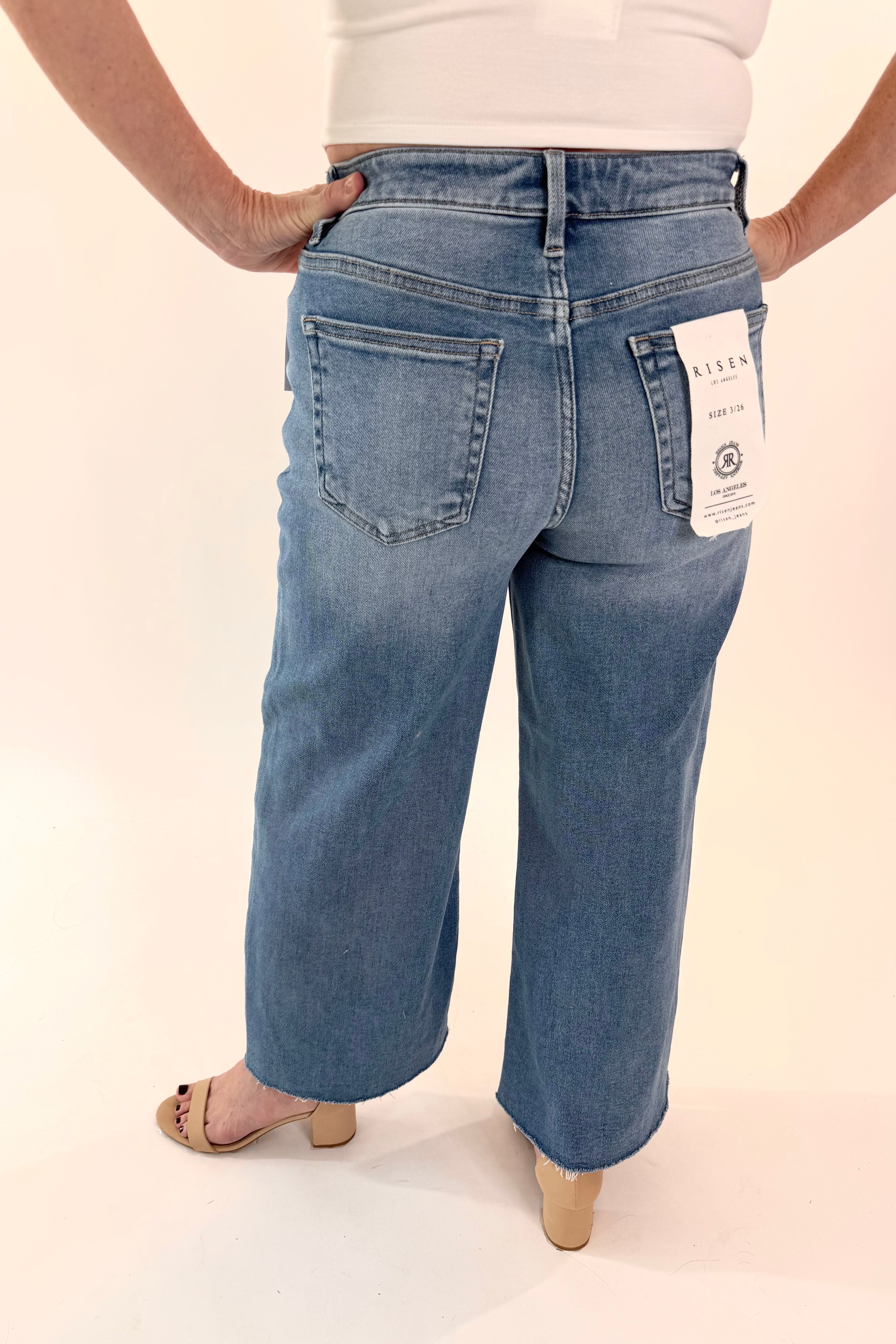 Person wearing blue jeans with a tag on a plain background