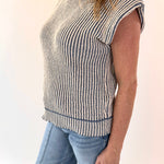 Person wearing a sleeveless striped top and jeans on a plain background
