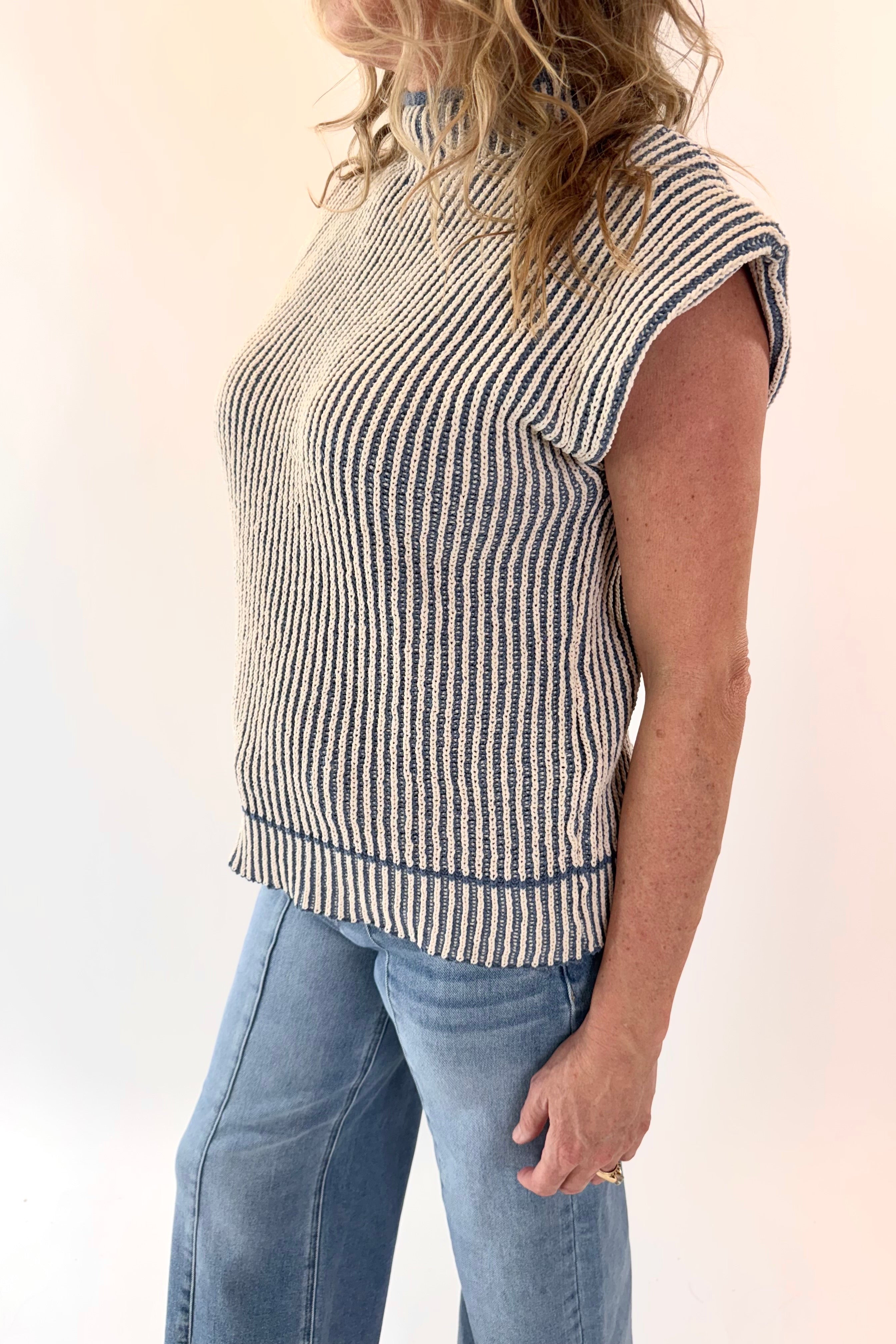 Person wearing a sleeveless striped top and jeans on a plain background
