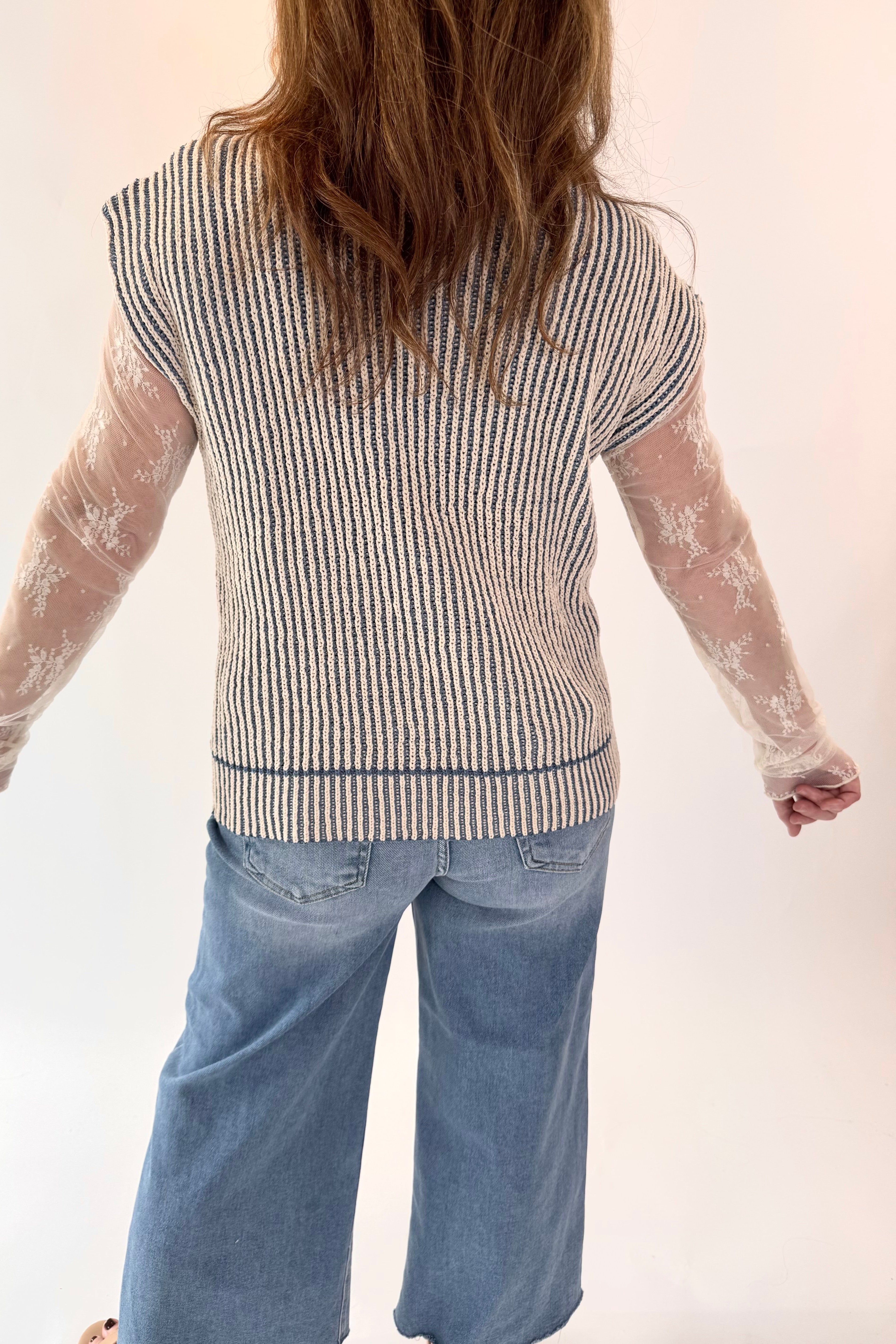 Person wearing a striped shirt with sheer sleeves and blue jeans on a white background