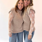Two women wearing matching outfits with sheer sleeves against a plain background
