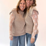 Two women wearing matching outfits with sheer sleeves against a plain background