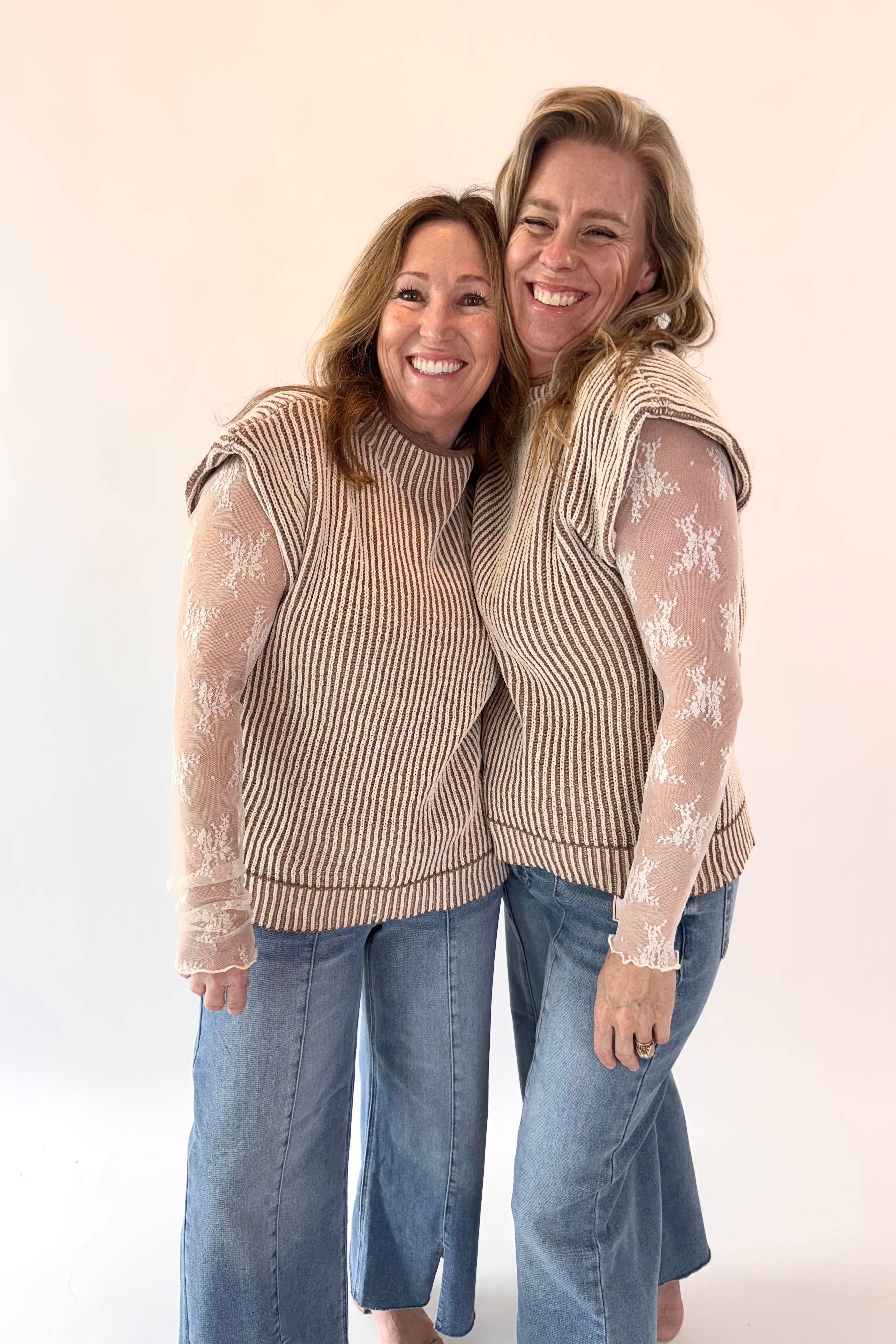 Two women wearing matching outfits with sheer sleeves against a plain background