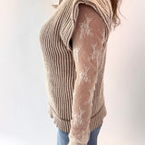 Person wearing a beige ribbed sweater over a sheer lace top with blue jeans on a white background