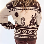 Person wearing a patterned sweater with cactus and cowboy design on a white background