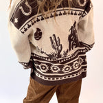Person wearing a patterned sweater with desert-themed designs on a white background