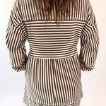 Person wearing a mocha and white striped dress on a plain background