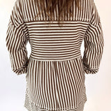 Person wearing a mocha and white striped dress on a plain background