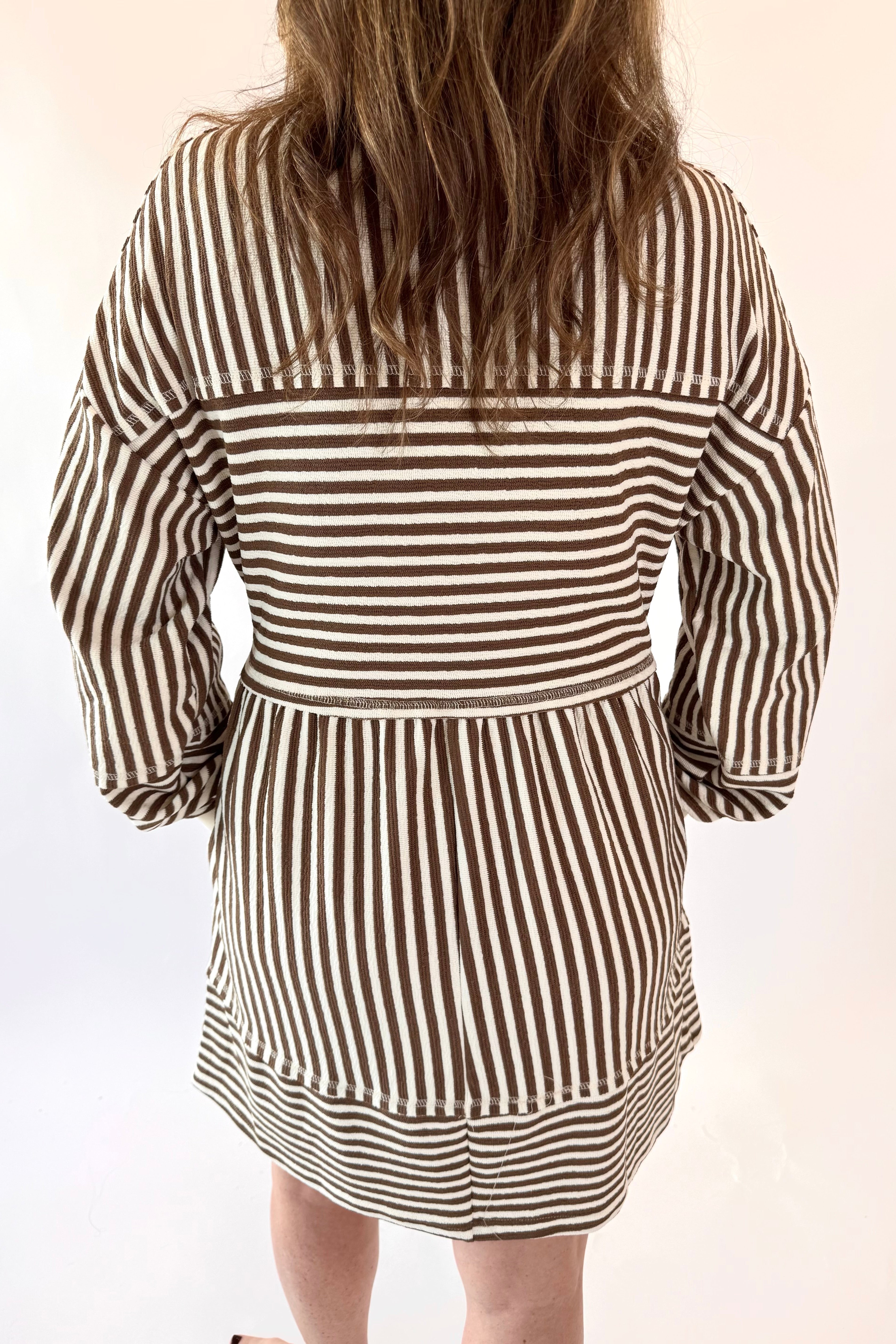 Person wearing a mocha and white striped dress on a plain background