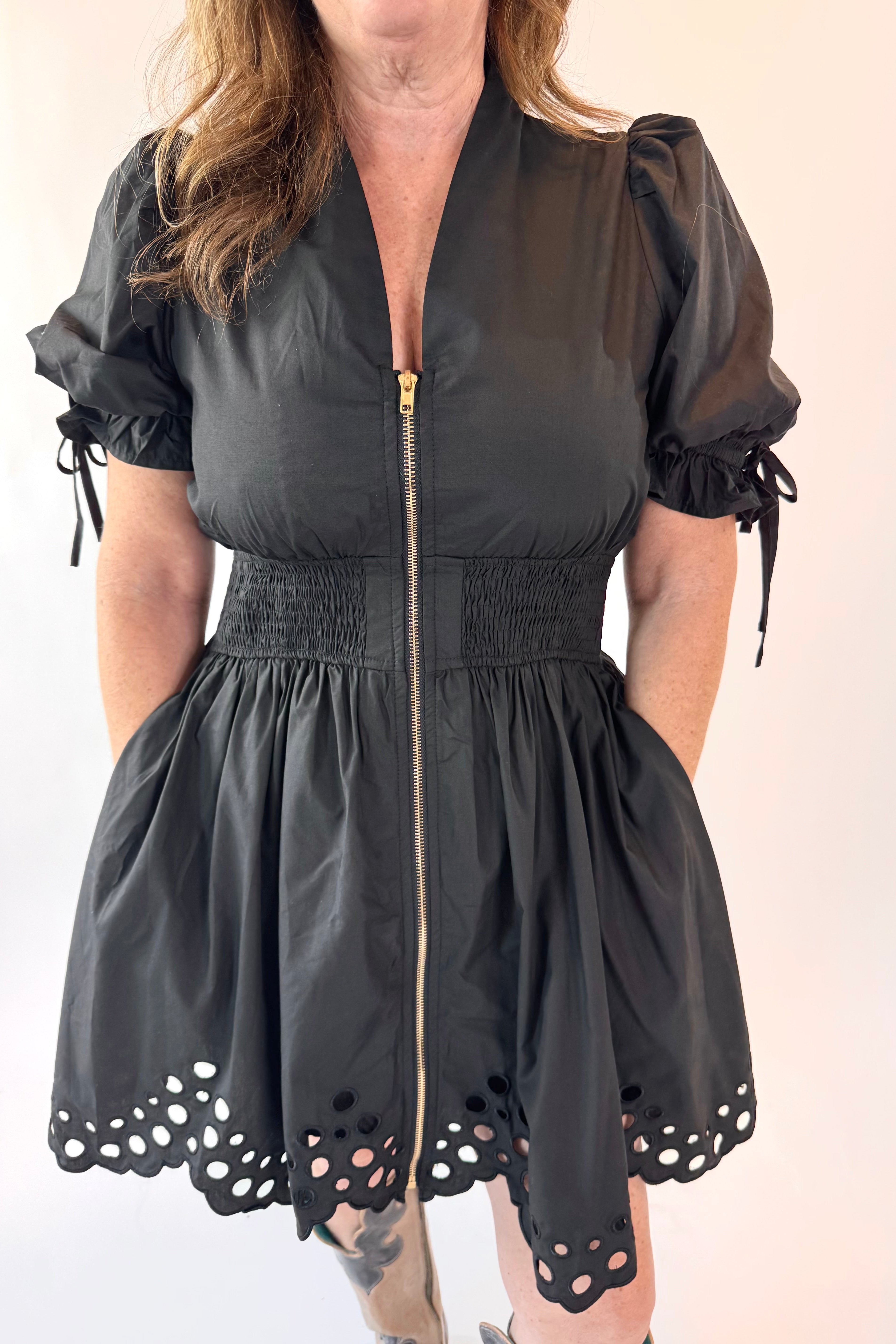 Black dress with puff sleeves and eyelet hem on a plain background