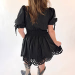 Child wearing a black dress with puff sleeves and lace details on a white background