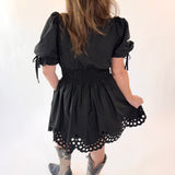 Child wearing a black dress with puff sleeves and lace details on a white background