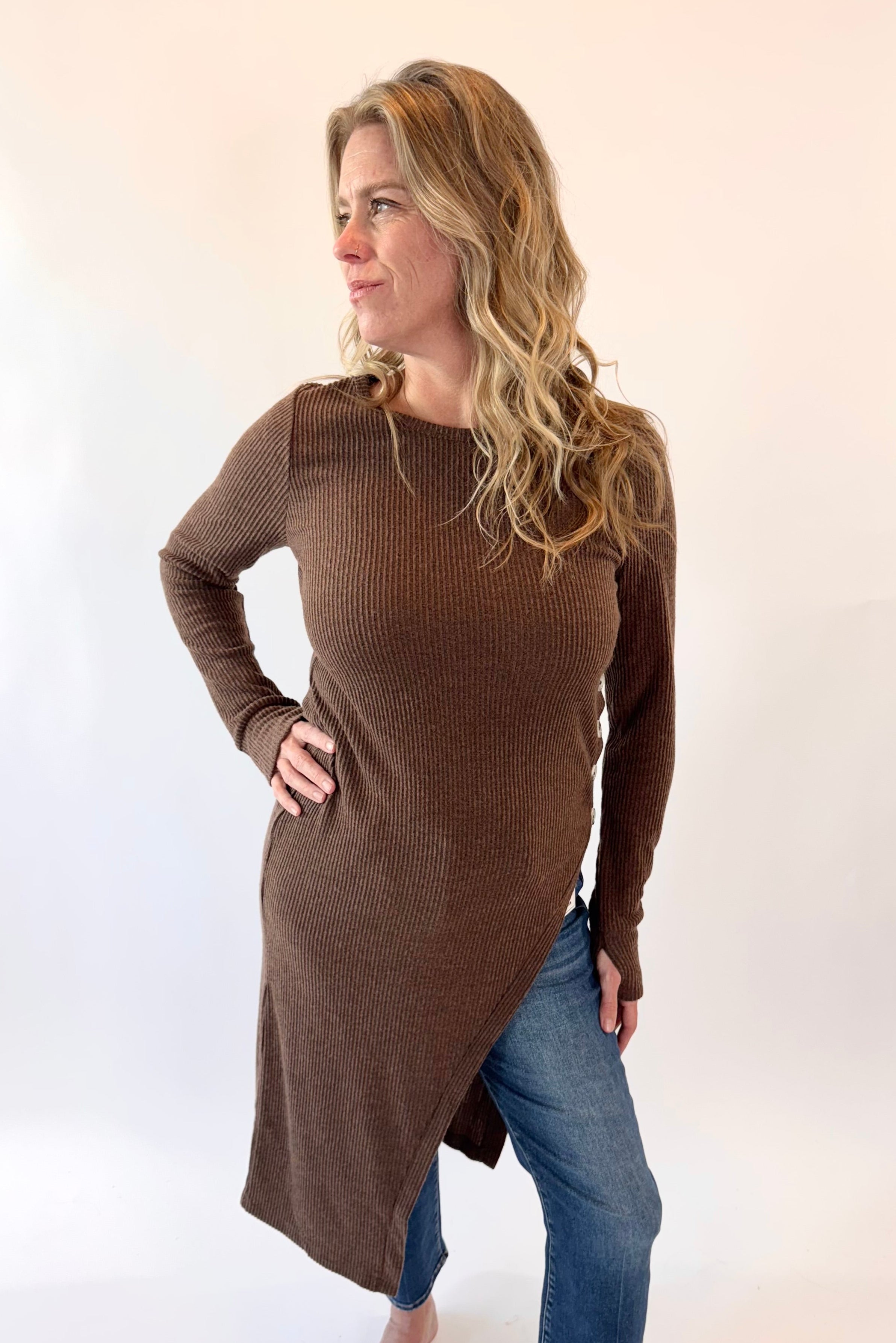 Woman wearing a brown long-sleeve top and blue jeans on a white background