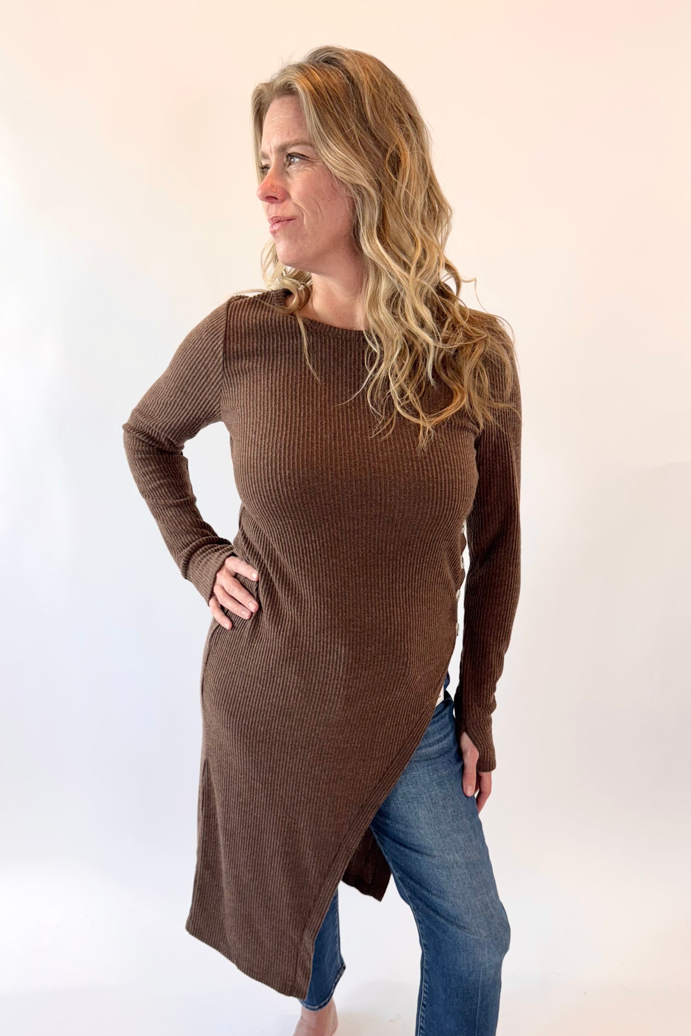 Woman wearing a brown long-sleeve top and blue jeans on a white background