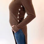 Person wearing a brown ribbed sweater with button details and blue jeans on a white background
