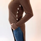 Person wearing a brown ribbed sweater with button details and blue jeans on a white background