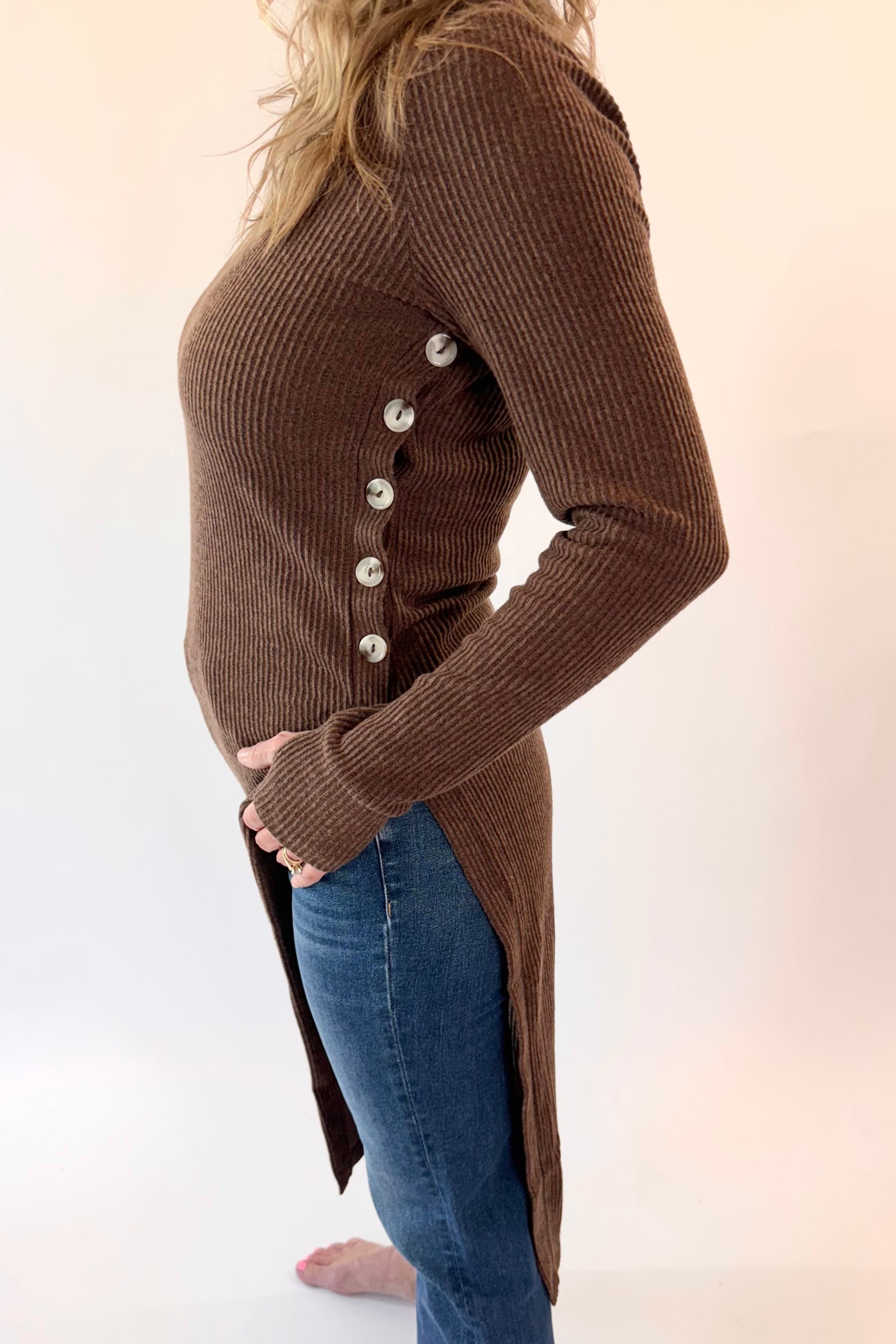 Person wearing a brown ribbed sweater with button details and blue jeans on a white background