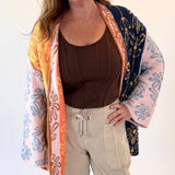 Woman wearing a colorful patterned cardigan over a brown top and beige pants on a white background