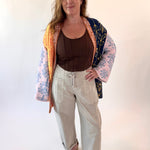Woman wearing a colorful kimono-style jacket over a brown top and beige pants on a white background