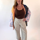 Woman wearing a colorful kimono-style jacket over a brown top and beige pants on a white background