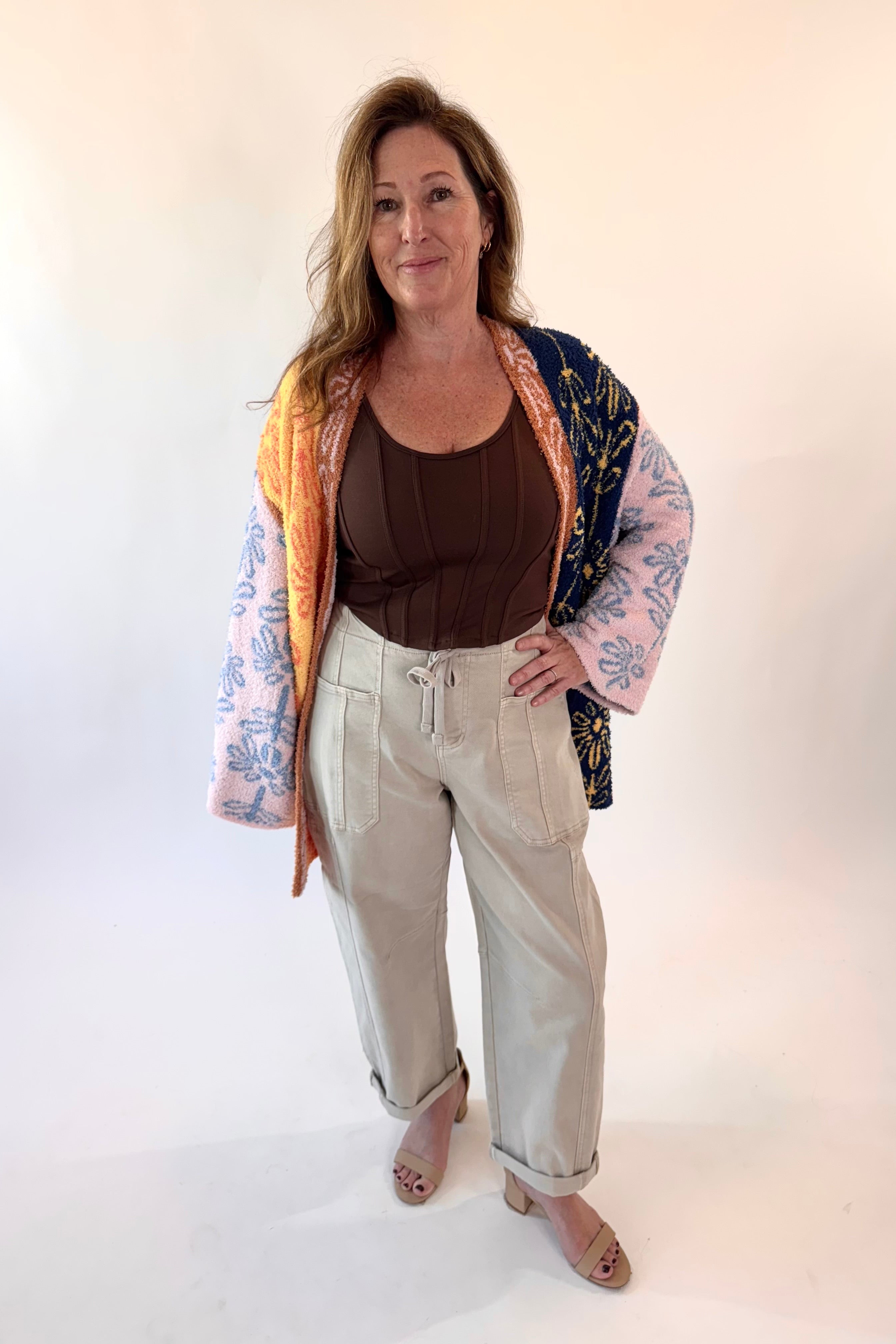 Woman wearing a colorful kimono-style jacket over a brown top and beige pants on a white background