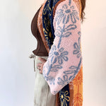 Person wearing a patterned cardigan over a brown top and beige pants on a white background