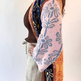 Person wearing a patterned cardigan over a brown top and beige pants on a white background