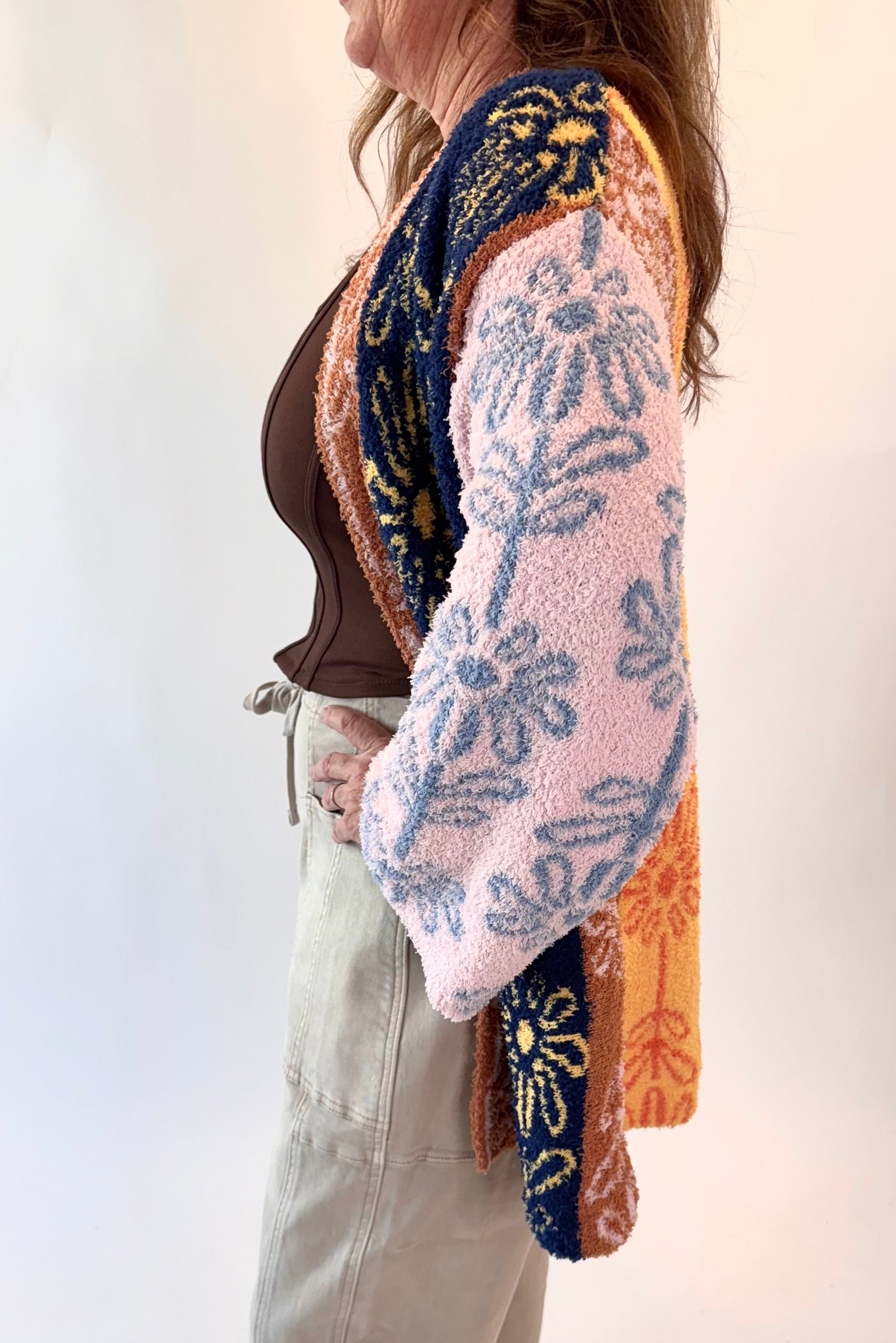Person wearing a patterned cardigan over a brown top and beige pants on a white background