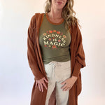 Woman wearing a green t-shirt with 'Kindness is Magic' text and a brown cardigan on a white background