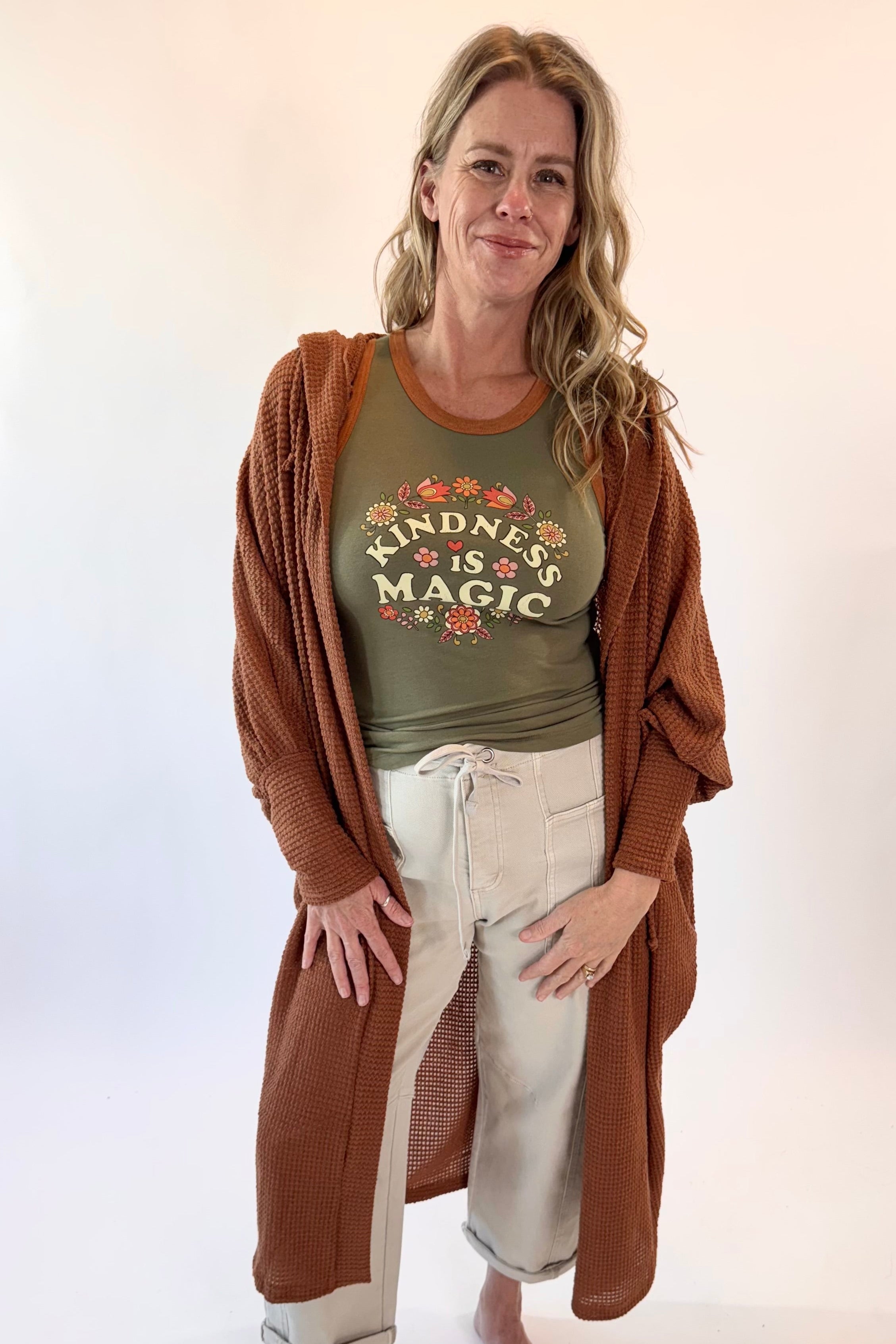 Woman wearing a green t-shirt with 'Kindness is Magic' text and a brown cardigan on a white background