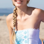 Woman on a beach wearing sunglasses and a light blue strapless top with a white towel draped over her shoulders.