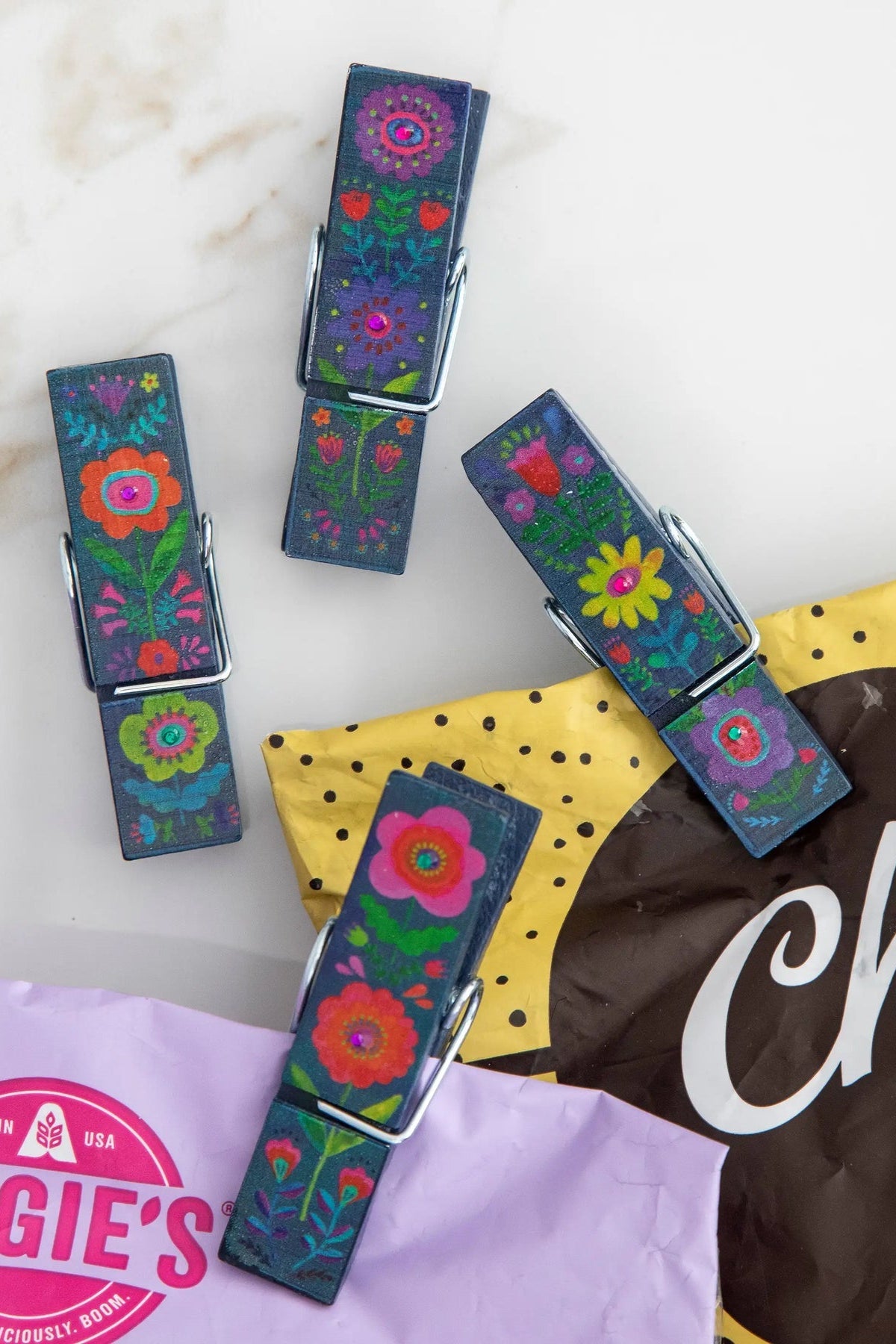 Colorful floral-patterned clips on a marble surface with a bag of chocolate in the background.