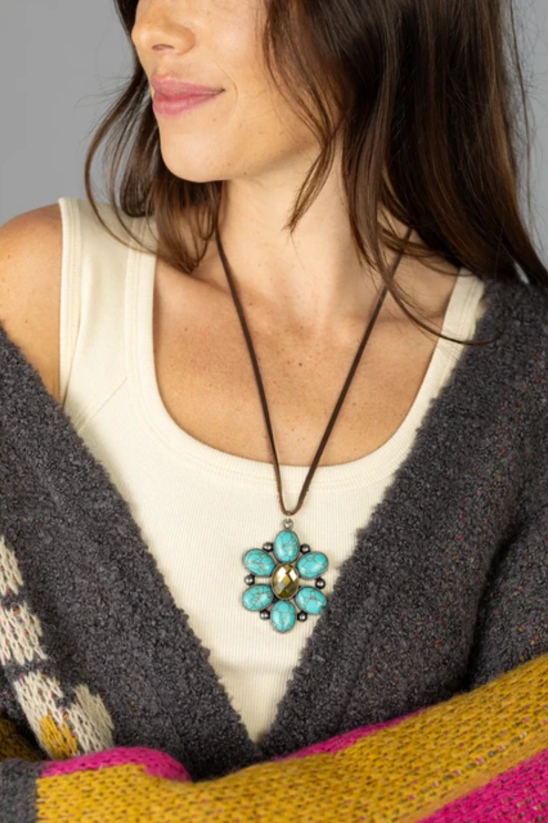 Woman wearing a necklace with a turquoise pendant against a neutral background