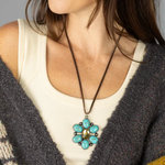 Woman wearing a necklace with a turquoise pendant against a neutral background