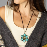 Woman wearing a necklace with a turquoise pendant against a neutral background