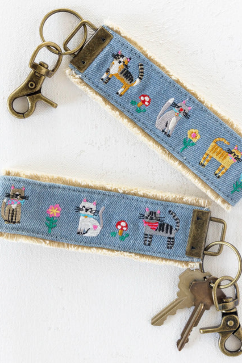 Denim key fob with embroidered designs of cats and flowers on a white background