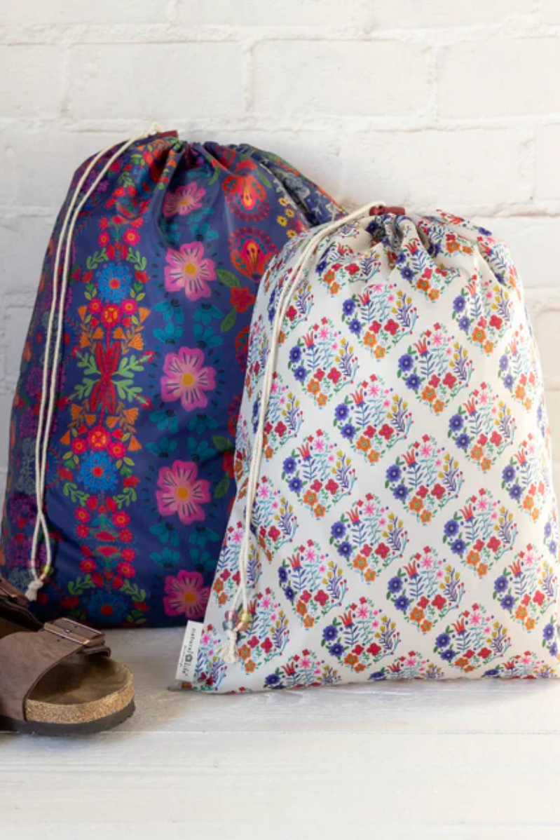 Two floral-patterned drawstring bags on a white surface with a brick wall background.