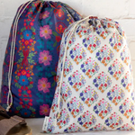 Two floral-patterned drawstring bags on a white surface with a brick wall background.