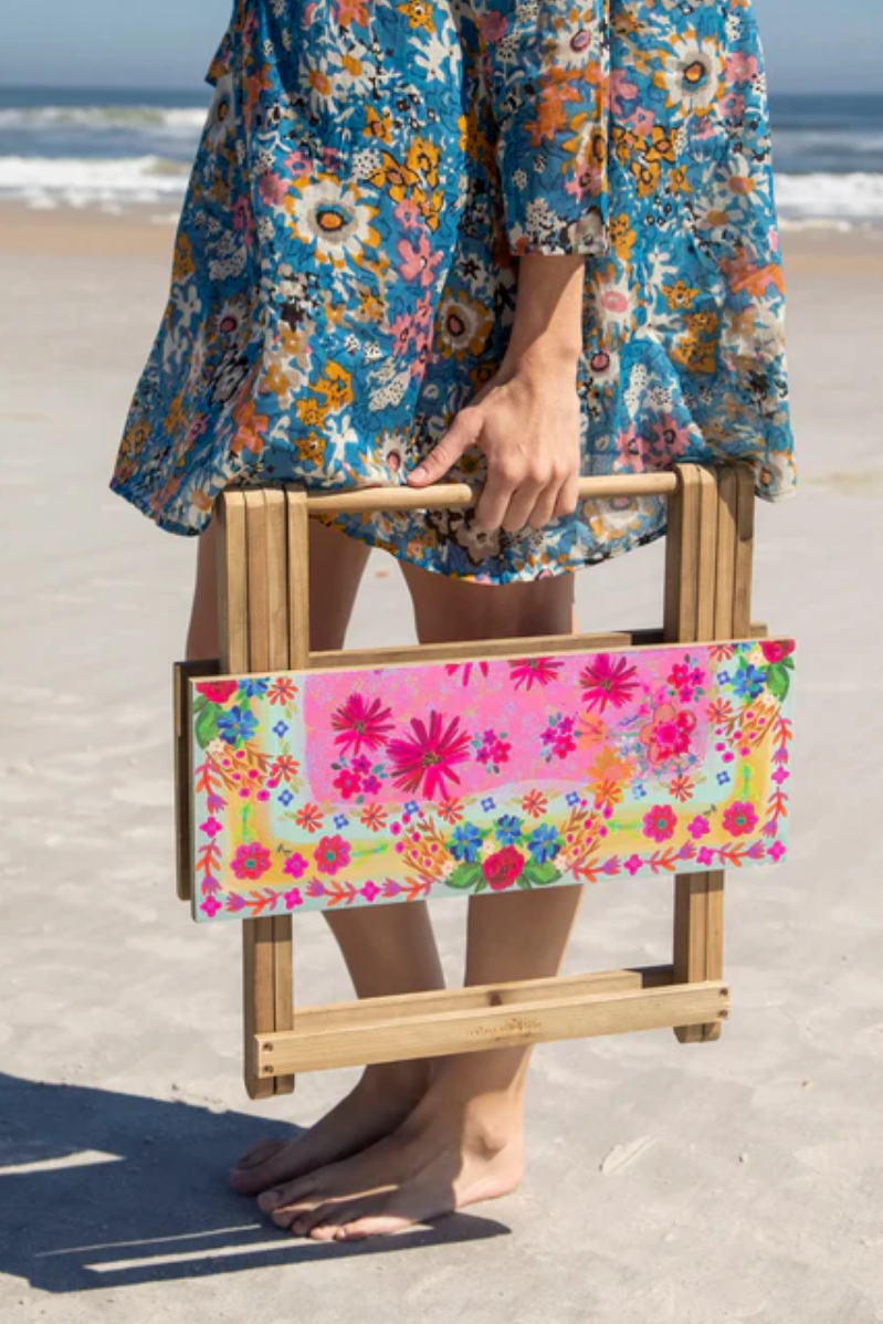 Person holding a floral-patterned folding chair on a beach