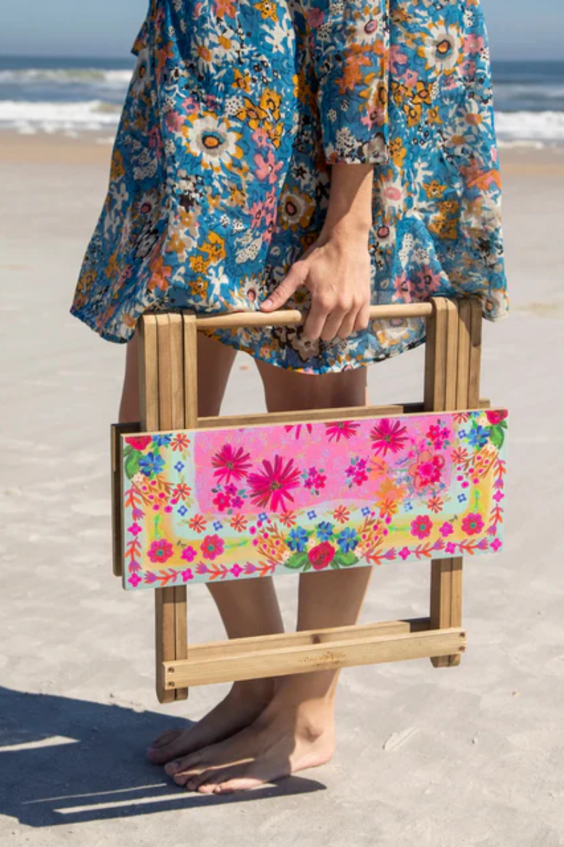 Person holding a floral-patterned folding chair on a beach