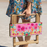 Person holding a floral-patterned folding chair on a beach