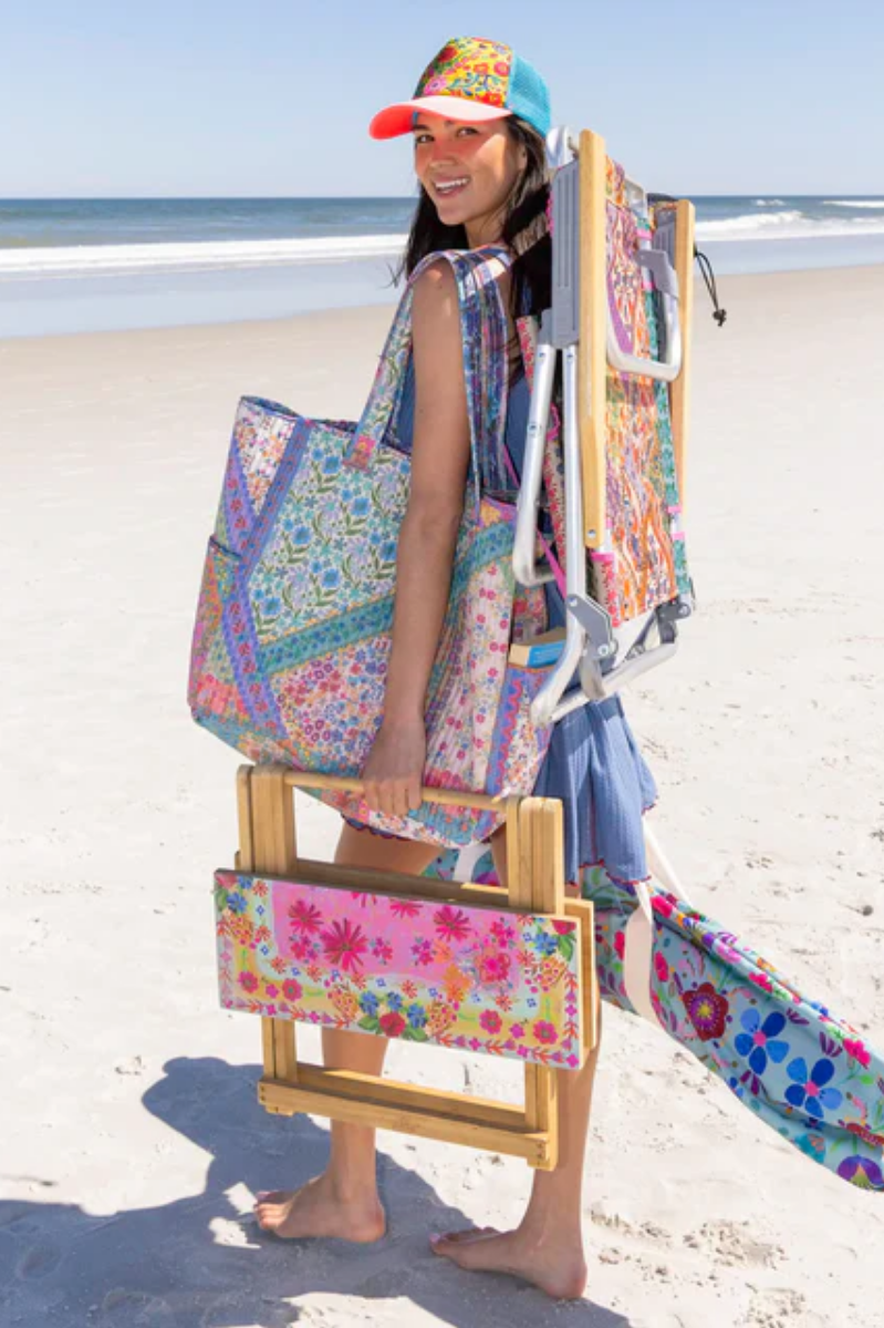 Woman on a beach with a colorful bag, chair, and hat.