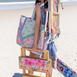Woman on a beach with a colorful bag, chair, and hat.