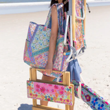Woman on a beach with a colorful bag, chair, and hat.