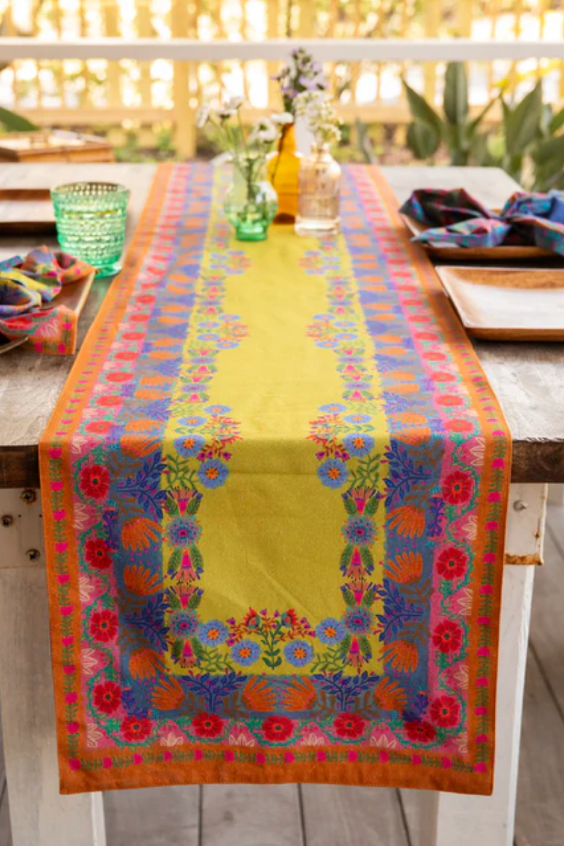 Colorful floral-patterned table runner on a wooden table with a blurred outdoor background.