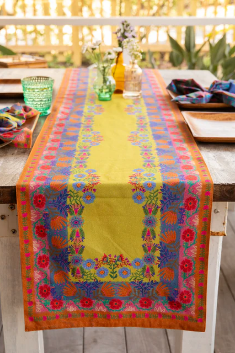Colorful floral-patterned table runner on a wooden table with a blurred outdoor background.