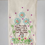 Decorative towel with floral embroidery and pom-pom trim on a wooden stick against a gray background